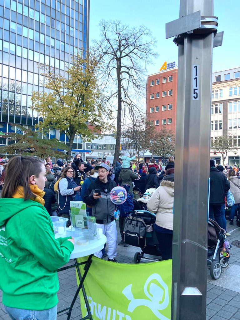 Infostand mit einer BDKJ-Mitarbeiterin auf einem Platz in der Innenstadt, sie schaut in die Menschenmenge.