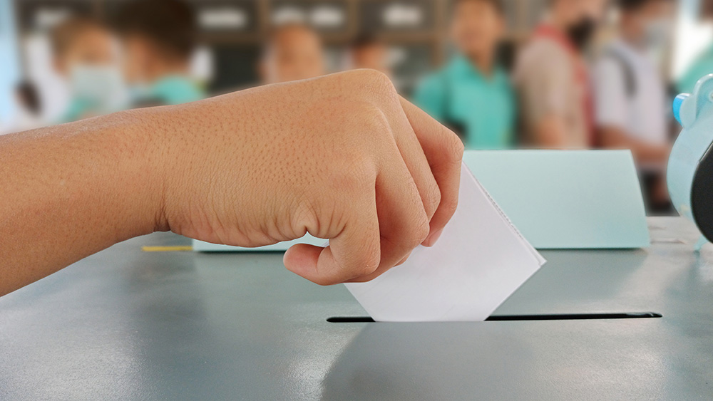 Das Bild zeigt eine Hand eines jungen Menschen, die einen Wahlzettel hält und diesen in eine Wahlurne wirft.